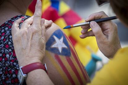 Una mujer pinta una bandera estelada en el brazo de otra antes de iniciarse la manifestación.