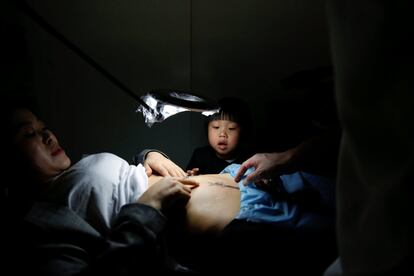 La hija mayor de Grace Yuan tiene tres años y mira la cicatriz en la barriga de su madre, debido a una cesárea. Un artista se la está tapando con un tatuaje en el local Samurai Tattoo en Shanghai, China.