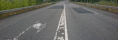 Tramo de carretera con marcas viales deterioradas, firme bacheado, con grietas longitudinales y roderas.