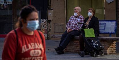 Dos personas mayores protegidas con mascarillas descansan sobre un banco en el barrio de Triana de Sevilla.