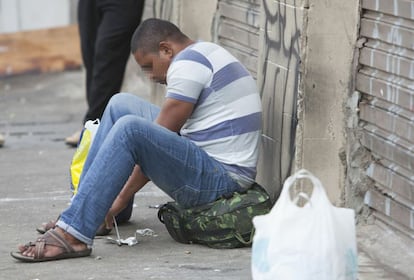 Um homem arruma seu cachimbo para fumar crack em uma das ruas da cracolândia. Para evitar o desconforto e a sujeira do chão, ele senta sobre uma mochila.