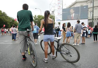 Dos jóvenes en bicicleta observan una de las pantallas la intervención del principe Felipe en la plaza de Cibeles.