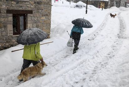 Dos personas caminan bajo una intensa nevada hoy en la localidad de Sotres, en el concejo de Cabrales (Asturias).
