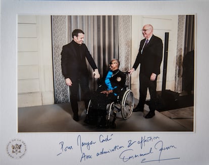 Maryse Condé junto a su marido y el presidente Emmanuel Macron en una fotografía de la presidencia de la Républica. Ceremonia de condecoración de la "Gran cruz de la orden del mérito nacional".