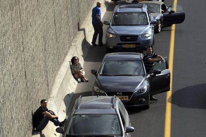 Un grupo de israelíes se cobija cerca de sus coches en una autopista mientras suena la alarma antiaérea en toda la ciudad de Tel Aviv (Israel) este miércoles.