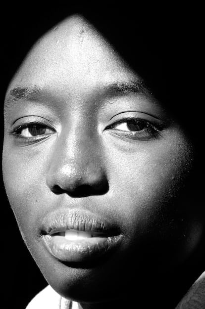 <p>El rostro de esta fotografía corresponde a Moussokura Colubaly, mujer procedente de Malí que reside en Recas, Toledo, “un pequeño y encantador pueblo que acoge la mayor concentración maliense de España”, describe Demian Ortiz (Madrid, 1981), autor de la imagen. Ortiz, que es fotoperiodista profesional, visitó esta localidad en 2012 junto al reportero Ramón Lobo para realizar un reportaje que se titularía ‘Mali, capital Toledo’. El objetivo era mostrar cómo esta comunidad seguía desde España, “con atención y angustiados”, las noticias que llegaban de la guerra en su país. “Mientras, desde aquí intentaban salir adelante en sus vidas, sufriendo a la vez la crisis económica y diversos problemas de racismo e integración”, explica Ortiz. De hecho, Moussokura contó a los periodistas que durante sus estudios en el instituto había sufrido episodios de discriminación. Por entonces tenía 19 años.</p> <p>Ortiz recuerda bien el momento en que tomó la imagen, merecedora de un accésit en la primera edición del concurso Africanas en España, en 2013: “Pudimos conocer a su maravillosa familia. Sus padres, hermanos y amigos nos acogieron con gran calidez y cariño. Guardo un gran recuerdo de los más pequeños, porque les llamaba mucho la atención mi cámara y me hacían un montón de preguntas divertidas mientras trabajaba”. A Moussokura la fotografió en su habitación con sus objetos más queridos. “Mientras me enseñaba algunas camisetas de futbol, me percaté de que por la claraboya entraba una luz muy especial. Le pedí que, simplemente, diese un paso hacia mí, me miró a cámara y disparé. El corte de luz que generaba la ventana dibujaba una sombra a la altura del pelo, a la vez que resaltaba su amplia sonrisa, y sobre todo, una mirada de esperanza y vida. Eso es lo que buscaba destacar porque es lo que encontré durante el reportaje en todas las personas que fotografié: las ganas de lograr una vida mejor en la que entre otras cosas, no seas juzgado nunca por el color de tu piel.</p> <p>Como fotógrafo experto en retrato editorial y reportaje, Ortiz ha publicado su trabajo en distintos medios de comunicación y ha publicado un libro de retratos en blanco y negro titulado ‘Perdidos. Un lugar para encontrar’ sobre la generación perdida de la literatura española.</p>