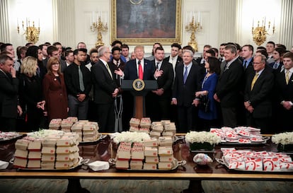 El presidente de Estados Unidos, Donald Trump, habla detrás de una mesa llena de hamburguesas de McDonald's, sándwiches de Chick fil-a y otras comidas rápidas mientras recibe a deportistas en la Sala Diplomática de la Casa Blanca, el 4 de marzo de 2019.
