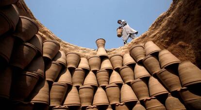 Un hombre porta una maceta de barro para colocarla junto a otras dentro de un horno en una fábrica improvisada de Peshawar (Pakistán).