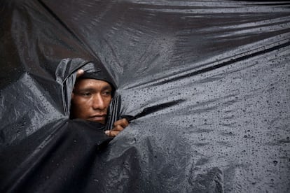 Un indígena Mbyá Guaraní se asoma por un agujero del plástico que lo protege de la lluvia que cae sobre la acampada que permanece enfrente del Instituto Paraguayo del Indígena para reclamar tierras para poder vivir.