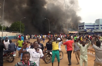 With the headquarters of the ruling party burning in the back, supporters of mutinous soldiers demonstrate in Niamey, Niger