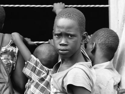 Una niño espera a entrar a la escuela en el campamento de Nyumanzi mientras mira a sus otros compañeros por la ventana del aula.