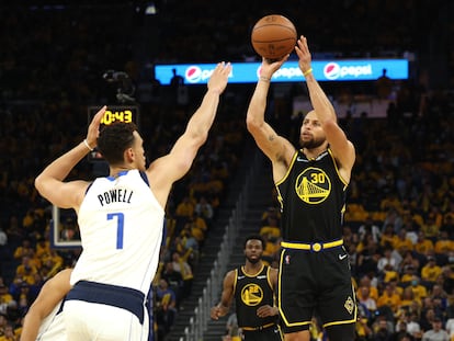 Stephen Curry, de negro, lanza a canasta esta madrugada ante la defensa de Dwight Powell (Dallas Mavericks).