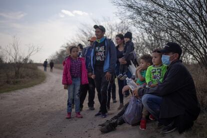 Un grupo de migrantes espera a lo largo de un camino de tierra para ser transportado después de cruzar el río Grande.