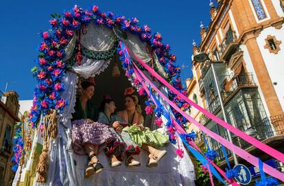 Tres mujeres subidas en una carreta en la salida de la Hermandad de El Rocío de Triana del popular barrio sevillano esta mañana hacia la aldea de El Rocío.