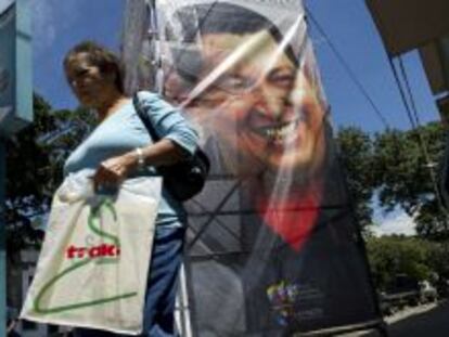 Una mujer camina frente a un poster de Hugo Chávez