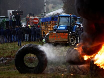 French farmers stand near tyres set on fire as they block the N12 road with their tractors to protest over price pressures, taxes and green regulation, in Plouisy, Brittany, France, January 24, 2024.