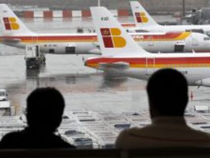 Dos pasajeros observan varios  aviones de la compa&ntilde;ia Iberia en las pistas de Barajas.