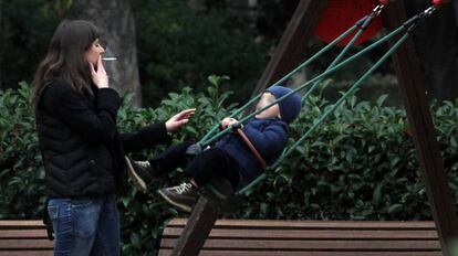 Una mujer fuma un cigarrillo ante un columpio ocupado por un niño en el parque del Retiro de Madrid.