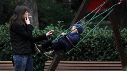 Una mujer fuma un cigarrillo ante un columpio ocupado por un niño en el parque del Retiro de Madrid.
