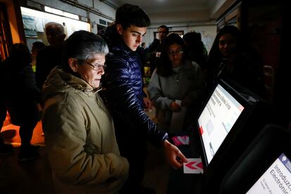 Un oficial electoral ayuda a una mujer mientras le muestra cómo usar el dispositivo electrónico para votar.