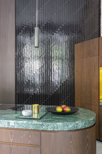 En la cocina, los armarios de castaño ahumado contrastan con las encimeras de mármol verde Guatemala y una pared de azulejos negros. Todo el enchapado está barnizado dejando el poro abierto, de este modo la madera es rica al tacto y el grano queda a la vista.