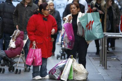 Dos mujeres conversan en el centro de Madrid ante varias bolsas cargadas de ropa recién comprada.