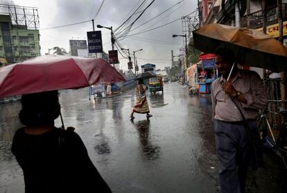 Varias personas caminan bajo la fuerte lluvia, en Calcuta (India).