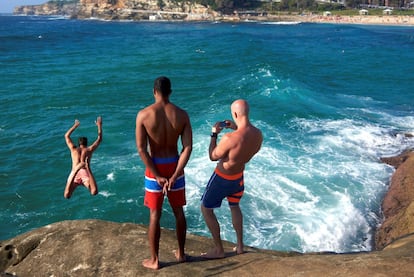 Un nadador salta de las rocas mientras dos personas observan cerca de la playa de Bronte, en Sydney (Australia).