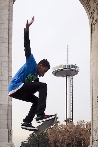 Un joven patina bajo el arco de la Victoria, con el faro de Moncloa cerrado al fondo.