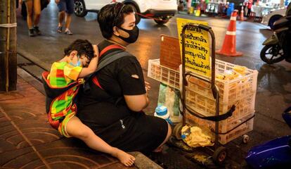 Una vendedora callejera espera clientes mientras su hijo duerme sobre sus espaldas en el barrio de Chinatown de Bangkok, Tailandia, el 21 de mayo de 2020.