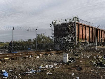 La policía húngara camina al lado de un vagón de ferrocarril cubierto de alambre en la frontera de Hungría con Serbia.