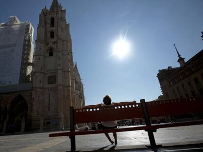 Una mujer toma el sol en un banco frente a la catedral de León.