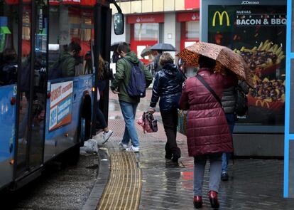 Usuarios de autobuses utilizan sus paraguas mientras esperan su turno para subir. 