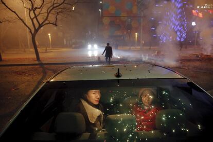 Una niña y una mujer permanecen sentadas dentro de un coche mientras que los petardos y los fuegos artificiales explotan con motivo de la celebración del inicio del Año Nuevo lunar, en Pekín (China), el 7 de febrero de 2016.