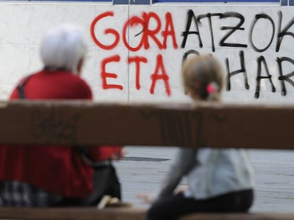 Dos personas sentadas ante una de las pintadas en favor de ETA, en Vitoria.