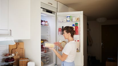 Una mujer sacando queso de un tupper que estaba dentro de la nevera.
