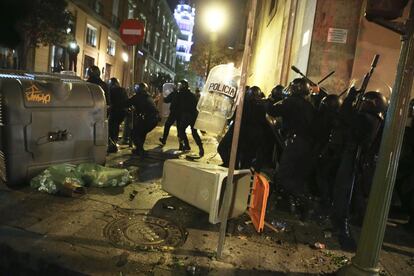 La polic&iacute;a carga y dispersa a los manifestantes en una calle con cubos de basura y contenedores de vidrio volcados. 