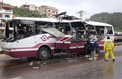 La policía israelí examina el autobús, reducido a chatarra.