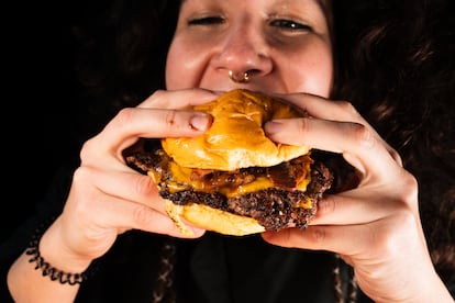 Primer plano de una joven comiendo y disfrutando de una deliciosa hamburguesa 'smash'.