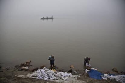 Lavanderos indios limpian ropa, mientras los pescadores reman en un bote en el río Brahmaputra en Gauhati (India).