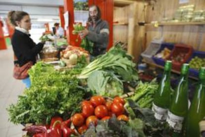 Un comerciante atiende a una clienta en su puesto de verduras ecológicas en el mercado de Vitoria. EFE/Archivo