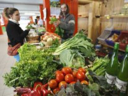 Un comerciante atiende a una clienta en su puesto de verduras ecológicas en el mercado de Vitoria. EFE/Archivo