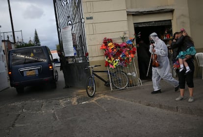 Un violinista con equipo de protección camina hacia un cementerio, mientras entra un coche fúnebre, en Bogotá (Colombia).