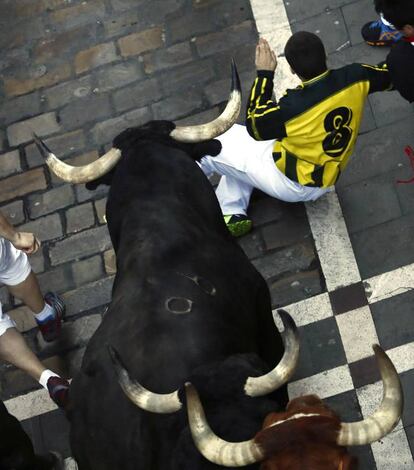 Un hombre se protege en el suelo ante el paso de los toros de la ganadería madrileña de Victoriano del Río, en la calle Estafeta.