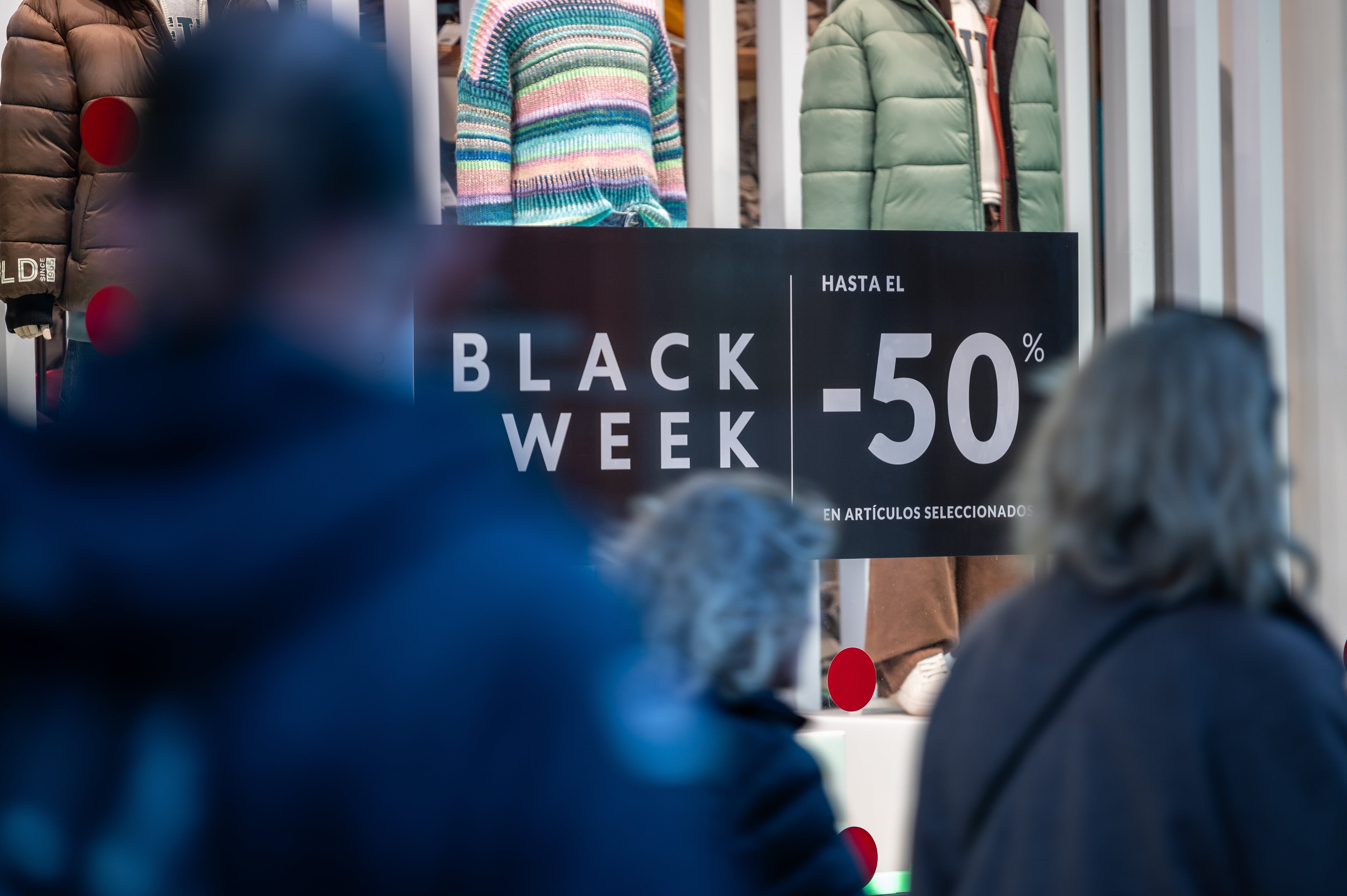 Gente camina por Madrid frente a una tienda con un cartel de ofertas del Black Friday en una imagen de archivo