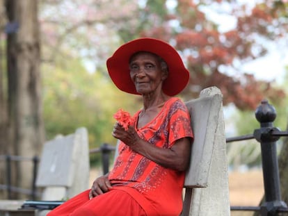 Una mujer mayor ataviada con sombrero disfruta en solitario de un día de sol en el Queen's Park Savannah, el principal parque de Puerto España (Trinidad y Tobago), pese a las restricciones y la orden de quedarse en casa.