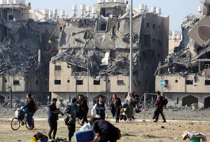 Un grupo de palestinos camina con sus pertenencias entre edificios destruidos por ataques israelíes, en Jan Yunis, este sábado.