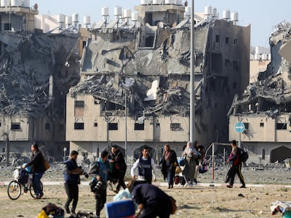 Un grupo de palestinos camina con sus pertenencias entre edificios destruidos por ataques israelíes, en Jan Yunis, este sábado.