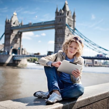 Una mujer consulta su tableta junto al T&aacute;mesis, en Londres, con el puente de la Torre (Tower Bridge) al fondo. 