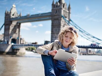 Una mujer consulta su tableta junto al T&aacute;mesis, en Londres, con el puente de la Torre (Tower Bridge) al fondo. 